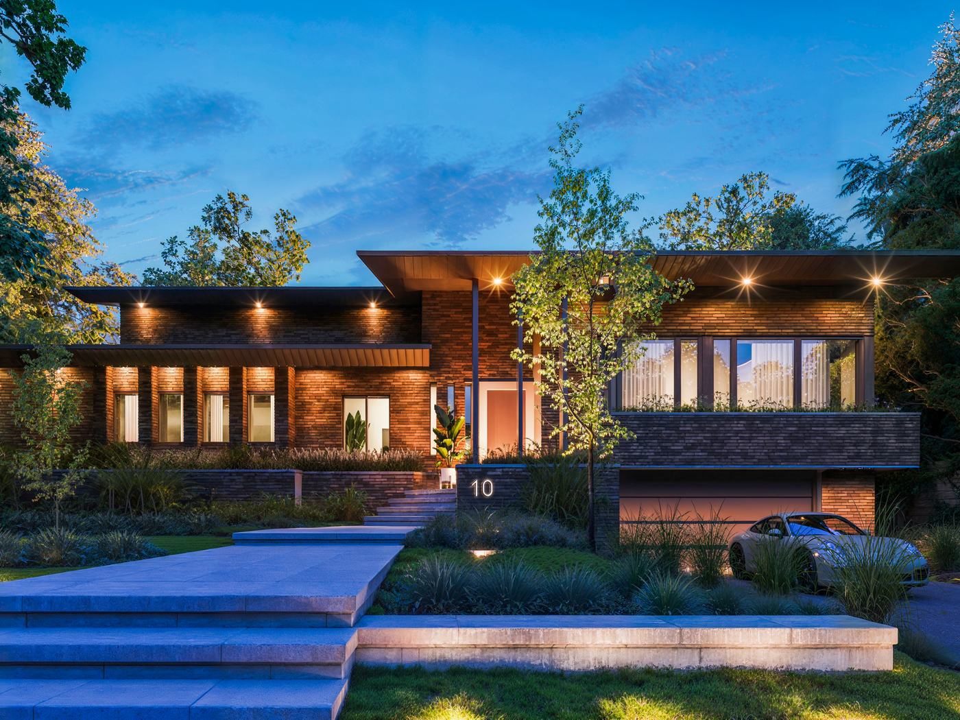 Une maison contemporaine de Montréal au crépuscule, fenêtres éclairées, vue depuis l’allée.